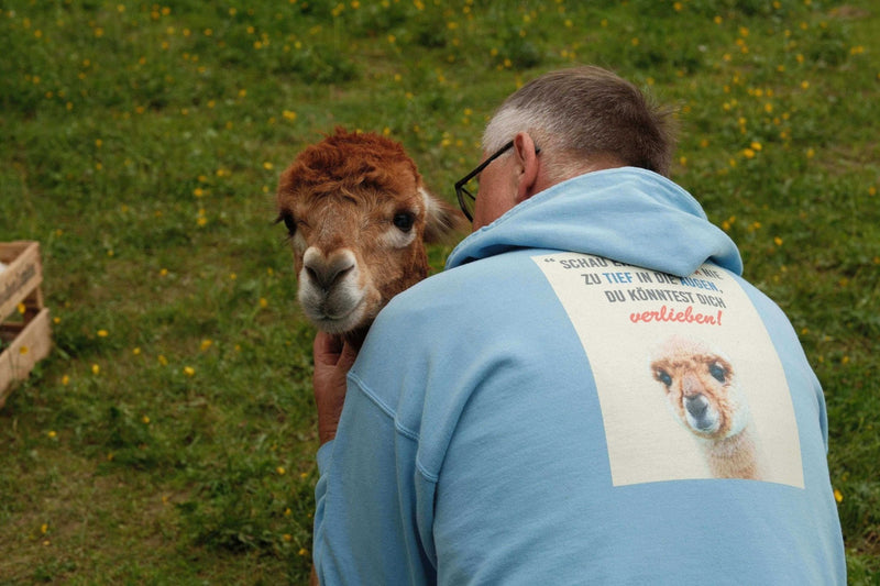 Wer wir sind – Unsere Liebe zu Alpakas & Flausch! Mann umarmt Alpaka bei natürlicher Umgebung.