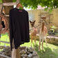 Schwarzer Alpaka Pullover Damen aus 100% Baby-Alpakawolle hinter Alpakas im Freien.