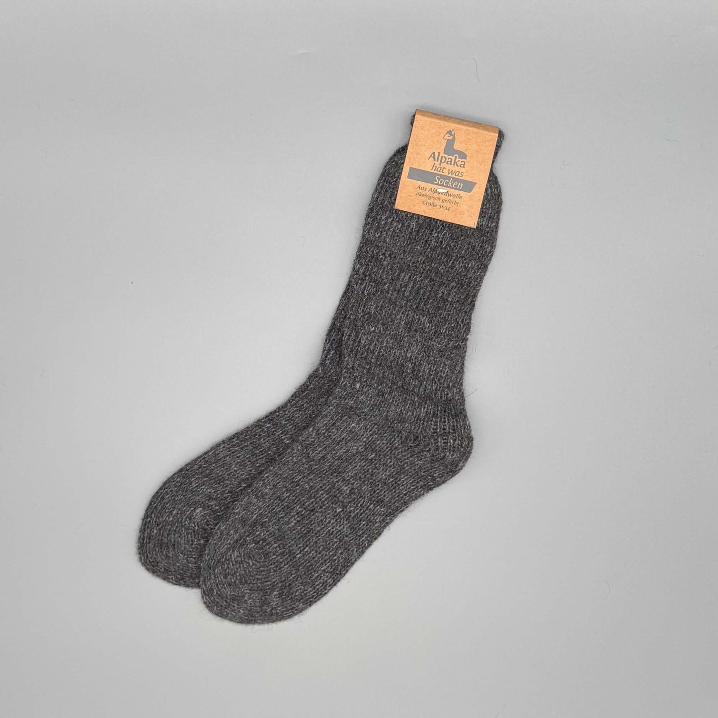 Alpaka Kindersocken aus 92% Alpakawolle in Grau liegend auf grauem Hintergrund.