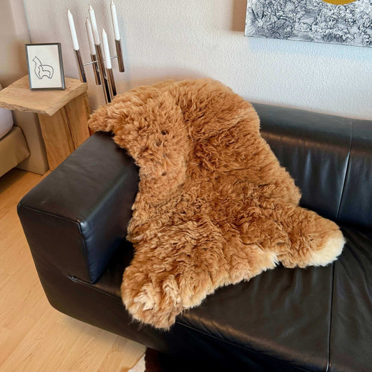 Handgefertigter Alpaka Fellteppich auf schwarzem Sofa, braun und weich, ideal als Wohnaccessoire.