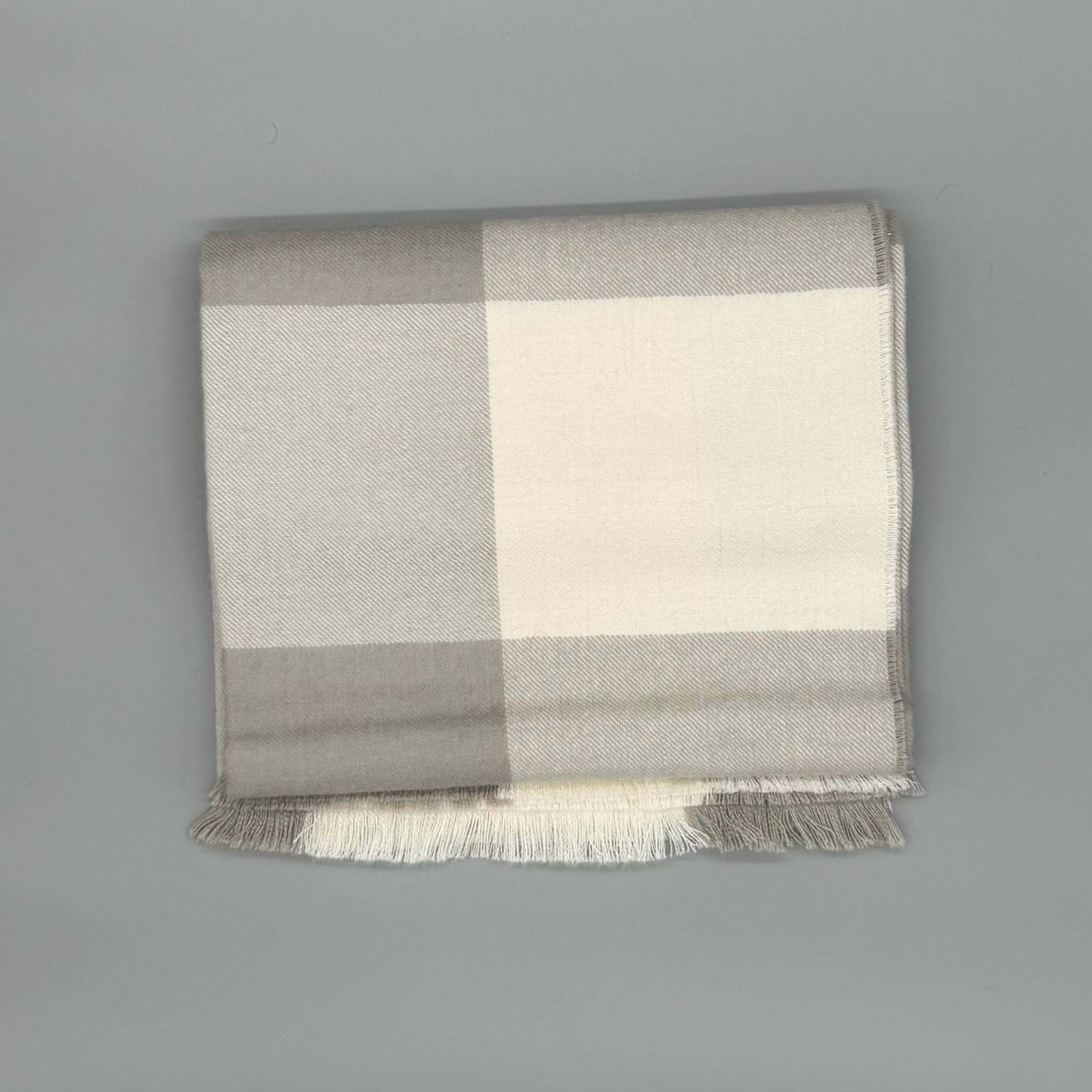 Flauschige Decke 130x180 cm aus 100% Babyalpakawolle im Karomuster in Blau und Grau auf grauem Hintergrund.