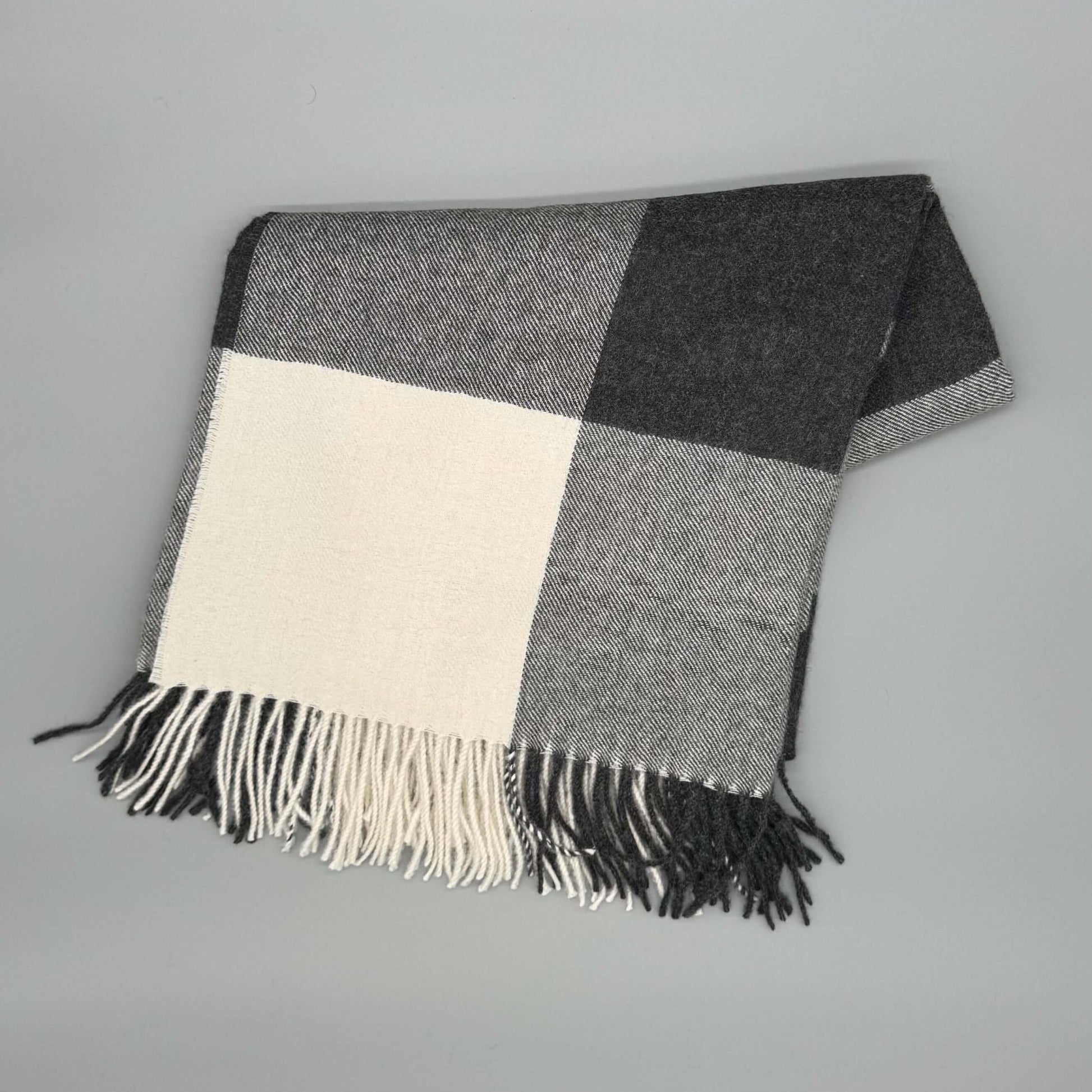 Flauschige Decke 130x180 cm aus 100% Babyalpakawolle im Karomuster (Blau, Grau) auf grauem Hintergrund.