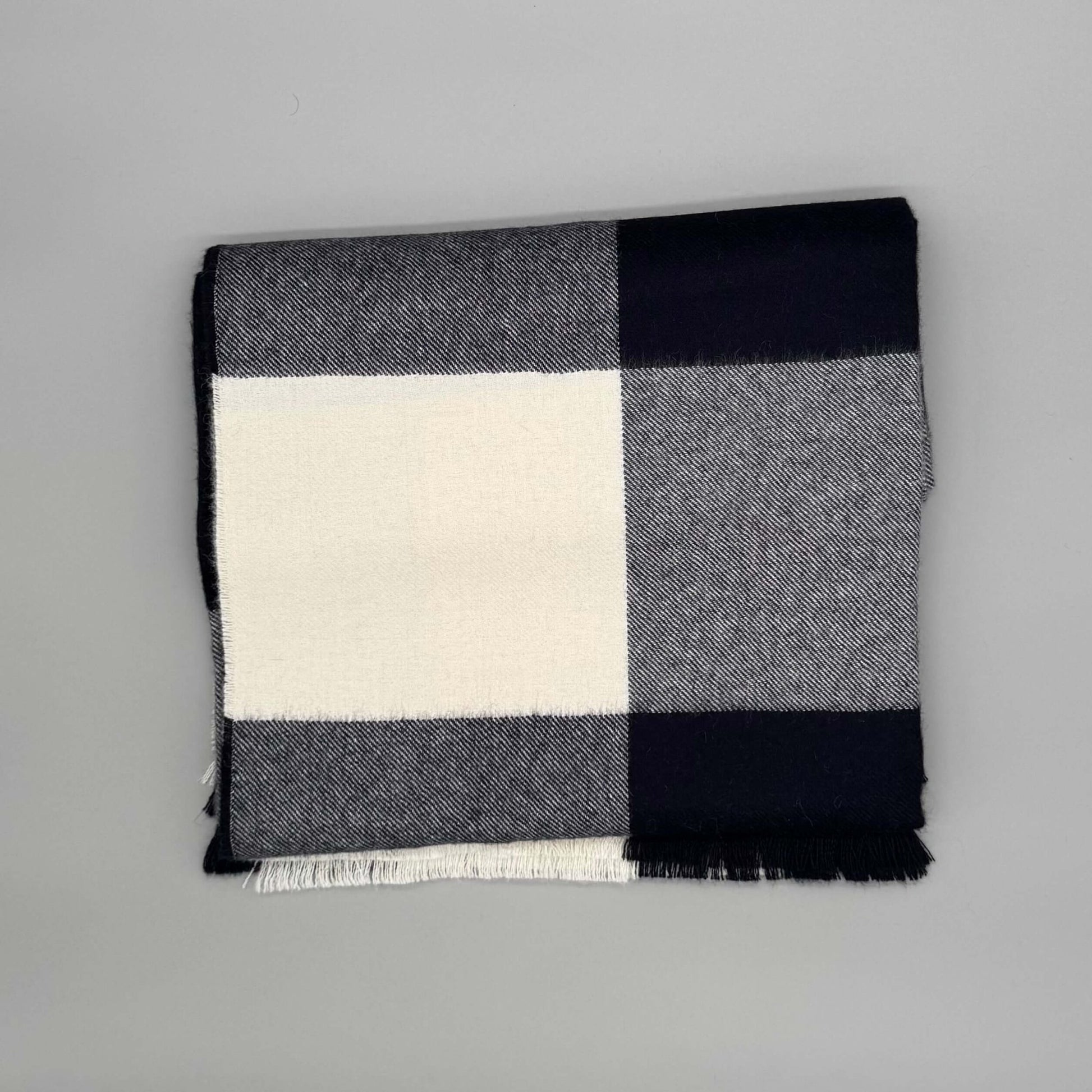 Flauschige Decke 130x180 cm aus 100% Babyalpakawolle im Karomuster (Blau, Grau) auf grauem Hintergrund.