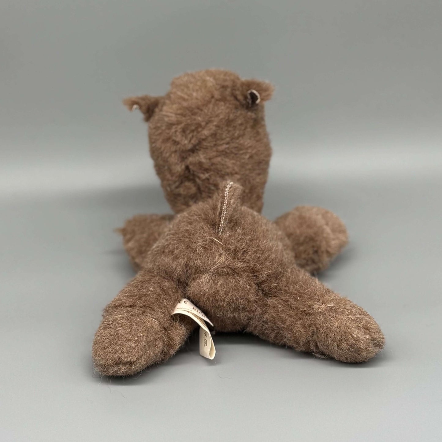 Alpaka Kuscheltier handgemacht aus 100 % Alpakawolle, braun, sitzend von hinten gesehen.